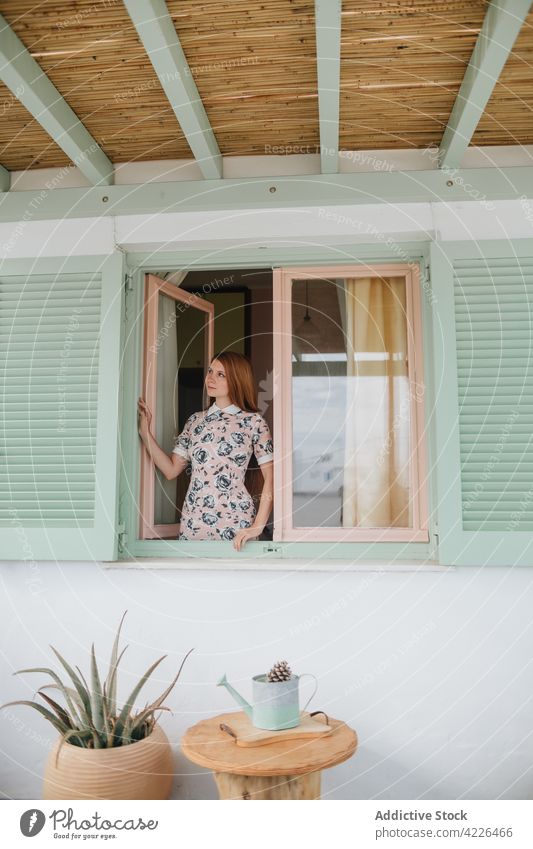 Dreamy woman standing near modern cottage facade house dreamy casual appearance young outfit calm unemotional sundress summer style adamantas milos emotionless