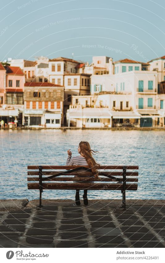 Anonymous woman resting on bench on old city embankment town historic canal promenade tourist sightseeing chania crete greece travel tourism architecture relax