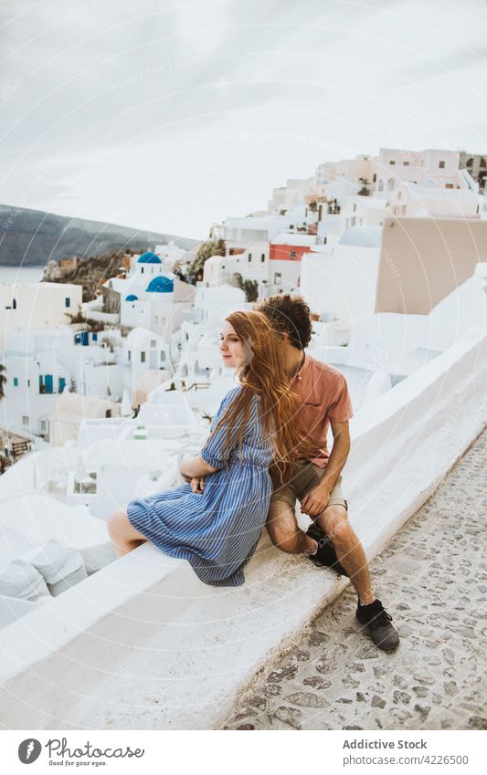 Young couple embracing on authentic coastal town street embrace traveler love romantic relationship seashore hug date holiday house affection resort oia village