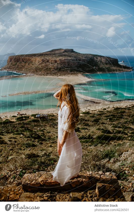 Unrecognizable woman standing on stony viewpoint against azure sea balos beach touch hair hilltop beachwear resort paradise picturesque admire scenic crete