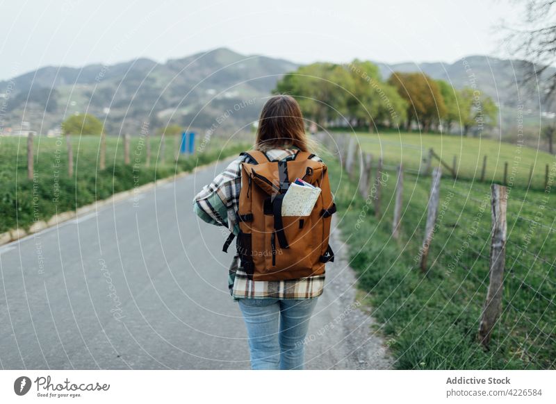 Unrecognizable backpacker with map walking on road against ridge hiker route direction rucksack highland woman countryside tourist wanderlust explore travel