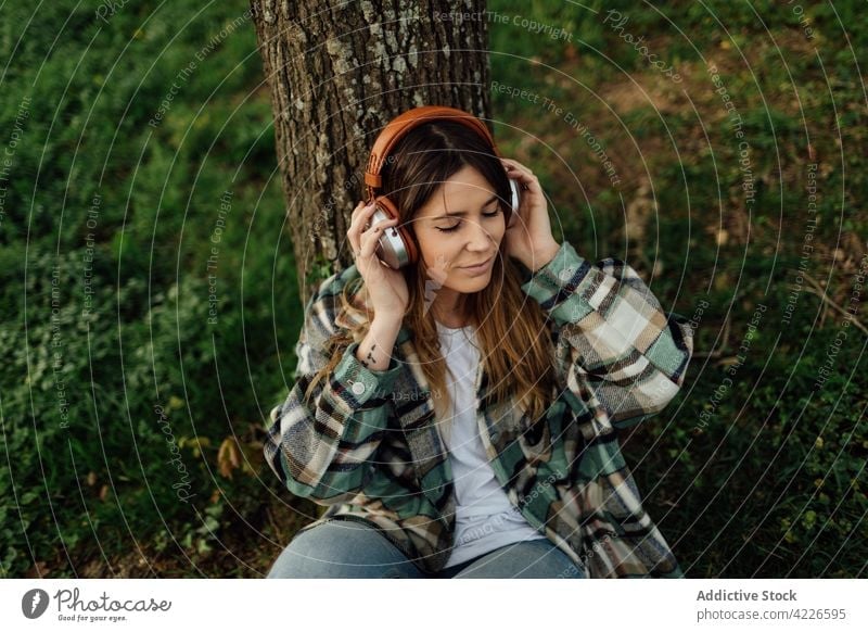 Smiling woman enjoying song from headset in countryside headphones music meloman listen smile melody using gadget device content tattoo millennial carefree tree