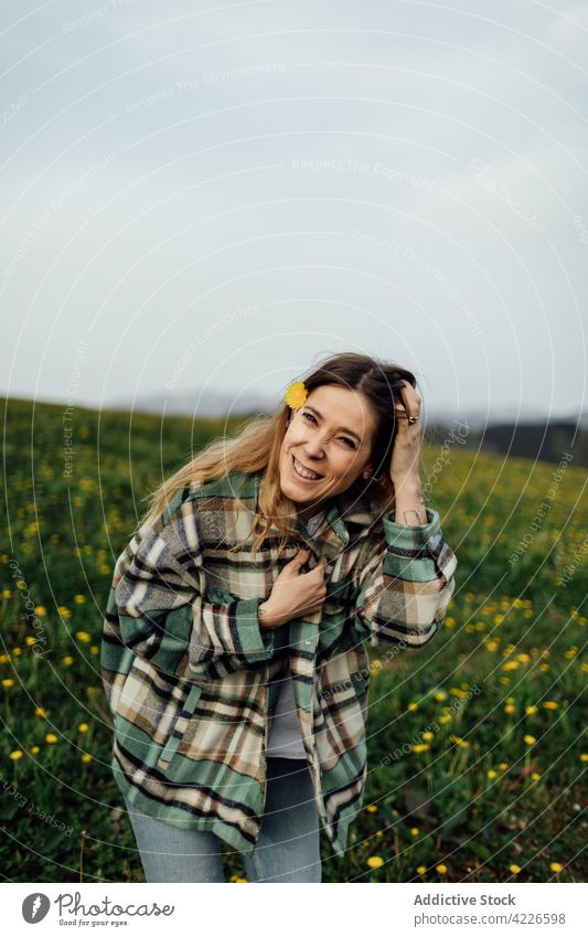 Cheerful woman touching hair in countryside field touch hair cheerful carefree enjoy gentle flower portrait smile glad content checkered shirt casual style