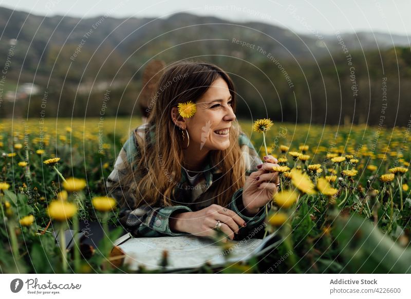 Happy tourist with map resting in field with blooming dandelions traveler smile vacation flower countryside woman blossom nature mountain trip enjoy content