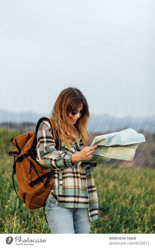Hiker with paper map in countryside field hiker itinerary trip wanderlust explore smile woman traveler feminine tourist sky guide orientate navigate rucksack