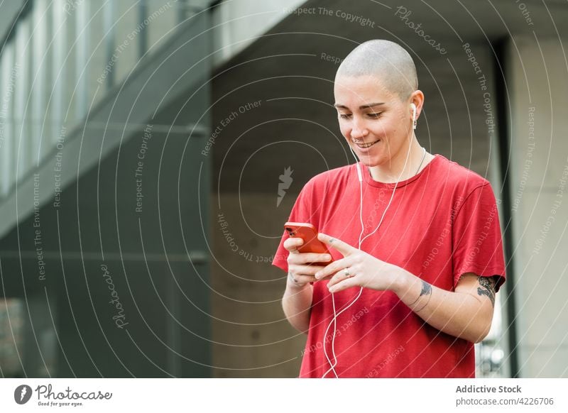 Lesbian woman with smartphone and tattoos on city street lesbian earphones accept listen happy music portrait using gadget device song androgynous smile audio