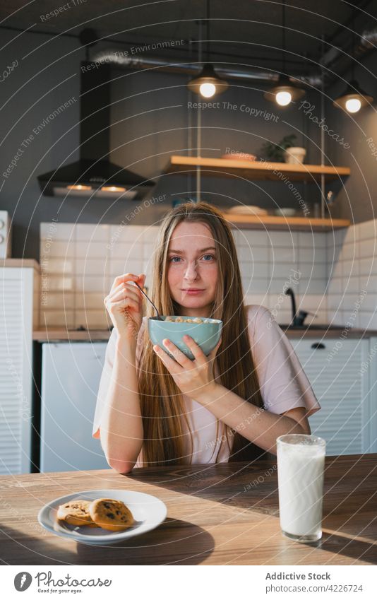 Woman eating delicious cereal for breakfast at home woman corn ring sweet nutrition portrait kitchen portion table domestic spoon bowl enjoy millennial friendly