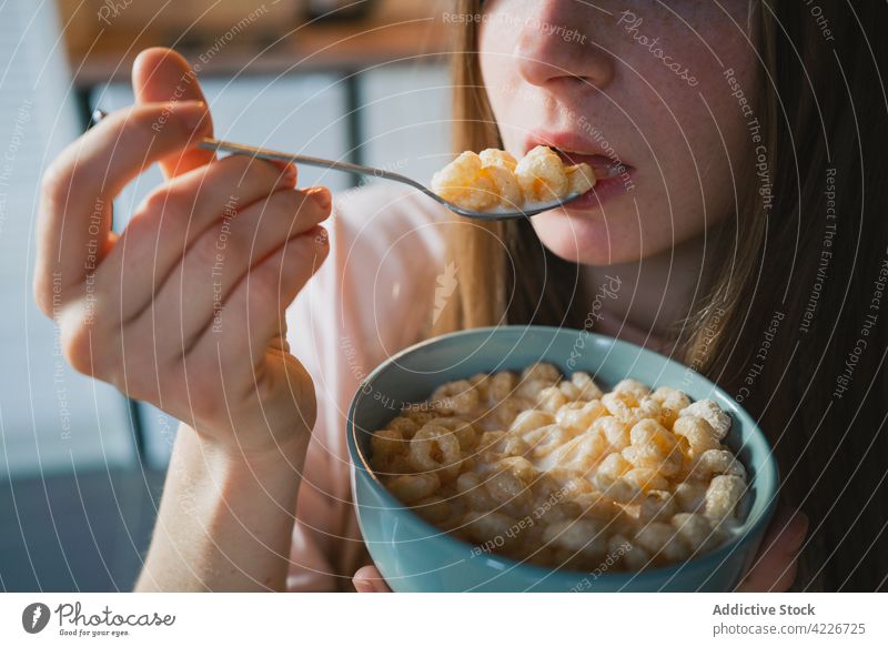 Crop woman eating delicious cereal for breakfast at home corn ring sweet nutrition portrait kitchen portion table domestic spoon bowl enjoy millennial friendly