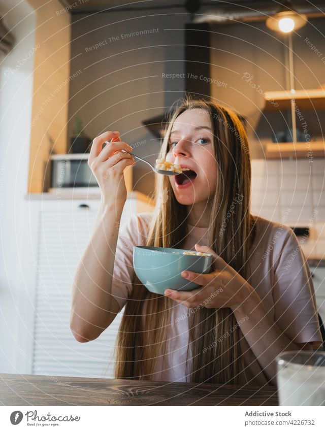 Woman eating delicious cereal for breakfast at home woman corn ring sweet nutrition mouth opened portrait kitchen portion table domestic spoon bowl enjoy