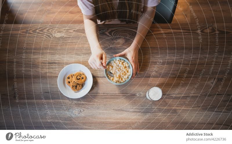 Crop woman with tasty cereal for breakfast at home cookie milk sweet nutrient baked table domestic glass biscuit oatmeal chocolate chip bowl corn ring delicious