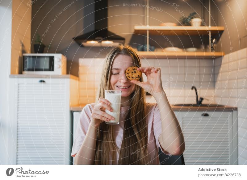 Smiling woman covering eye with oatmeal cookie in kitchen cover eye milk breakfast cheerful sweet treat eyes closed dreamy concentrate smile content glad glass