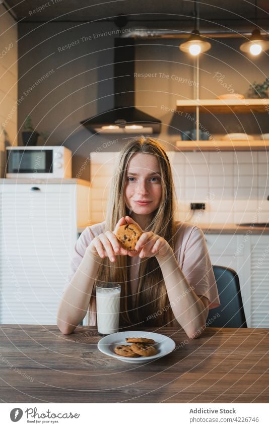 Smiling woman with delicious oat cookie at home treat chocolate chip sweet baked breakfast smile cheerful kitchen content glad scent beverage milk glass drink
