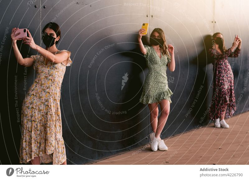 Unrecognizable girlfriends in masks taking selfie on smartphones in city feminine anti social memory moment millennial obsession problem town using gadget women