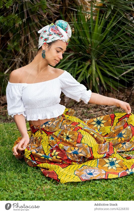 Black woman in traditional apparel on lawn cheerful ornament style friendly tropical palm garden portrait african content smile glad skirt blouse culture