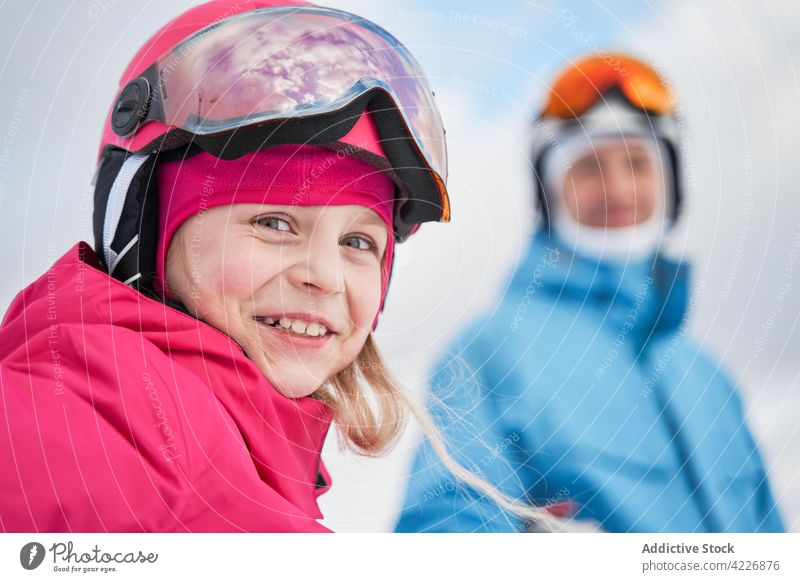 Happy girl in ski helmet standing near parent in nature activewear sport snowy father training vitality toothy smile terrain cheerful winter season energy