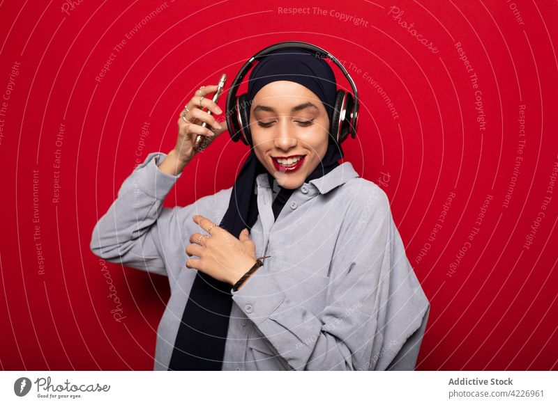 Cheerful Muslim woman in headphones listening to music on mobile phone cheerful dance muslim meloman happy casual device gadget wireless enjoy young hijab sound