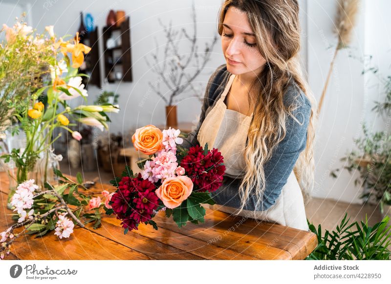 Focused young female florist creating composition with assorted fresh flowers woman bouquet rose work plant floral workplace arrangement occupation decor casual