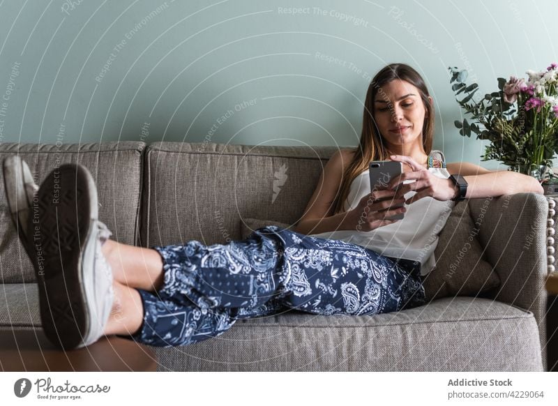Woman chatting on smartphone on sofa at home woman spare time weekend internet legs crossed house using gadget device lifestyle cellphone text messaging