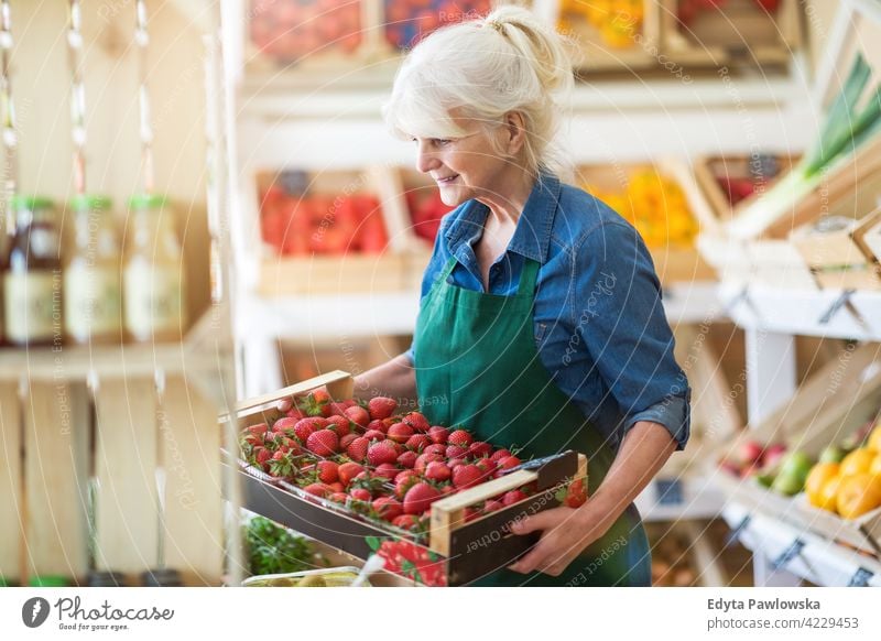 Senior woman working in small grocery store greengrocer groceries people senior mature adult casual attractive female smiling happy Caucasian toothy enjoying