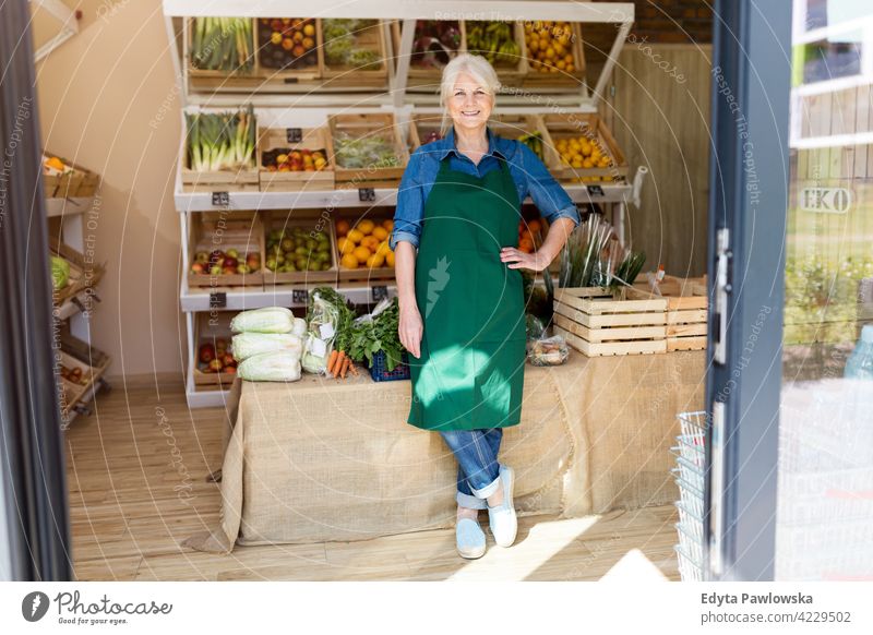 Senior woman working in small grocery store greengrocer groceries people senior mature adult casual attractive female smiling happy Caucasian toothy enjoying