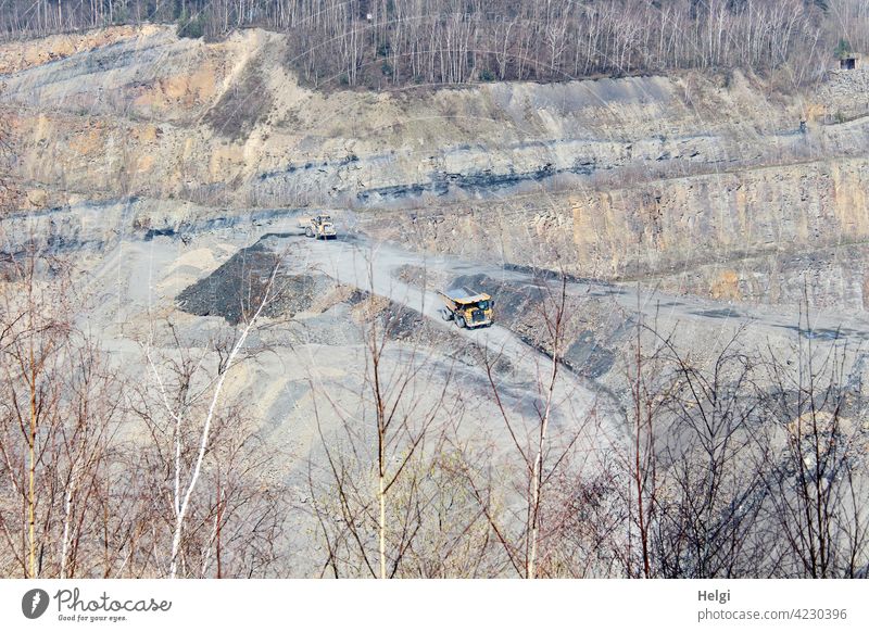 View into a quarry , a truck and a wheel loader on the transport routes Quarry stone rock strata Sandstone Hard Shale argillaceous schist Slate Industrial plant