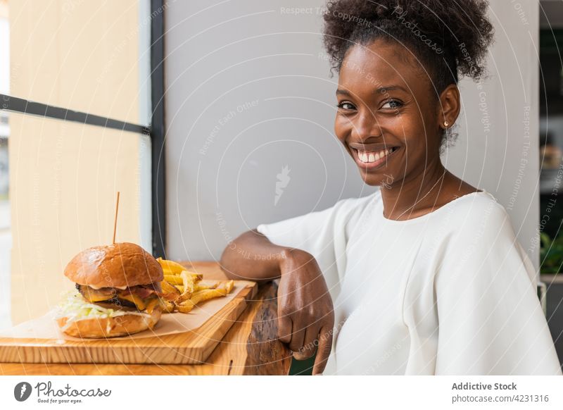 Black woman enjoying fries and burger in restaurant eat hamburger appetizing delicious fast food glass wall tasty meal junk food yummy hungry serve lunch dish