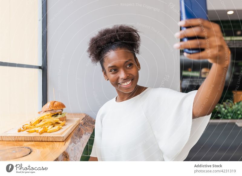 Happy black woman eating fries and taking selfie burger joyful smartphone restaurant cheerful take photo bite delicious lunch device positive young meal