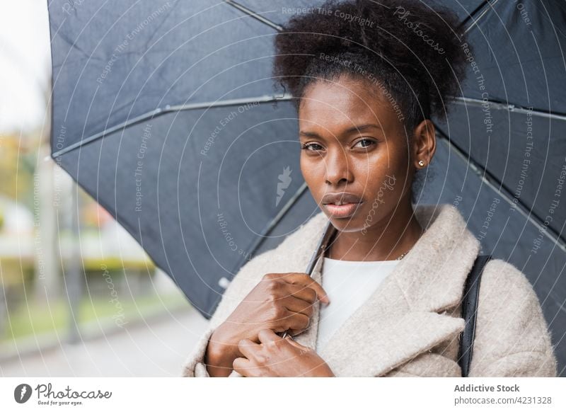 Stylish black woman with umbrella standing on city street outerwear style trendy outfit street style cool modish appearance look modern warm clothes urban young