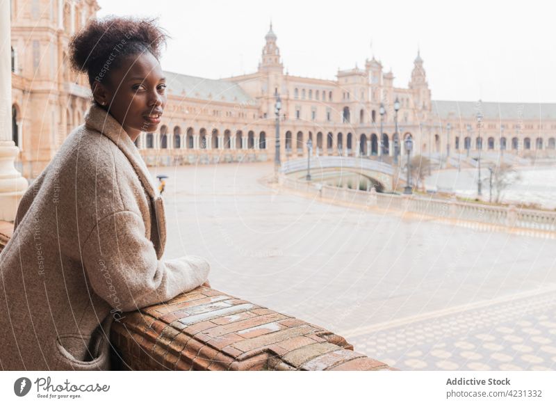 Black woman standing near historic majestic palace in old city admire architecture column sightseeing landmark attract seville spain trip tourism exterior