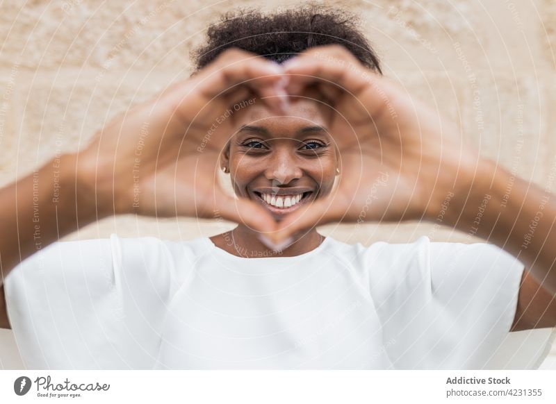Joyful black woman showing heart sign and smiling gesture toothy smile happy love carefree like valentine romantic optimist cheerful glad expressive pleasant