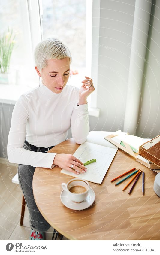 Astrologer writing in notebook at table in house astrologer write predict future horoscope astrology pseudoscience woman shiny take note paper coffee stationery