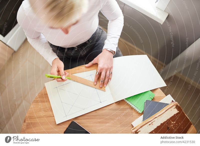 Crop astrologer drawing on paper at desk in house triangle geometry prepare astrology woman home pseudoscience divine predict future table astrologist pen