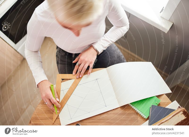 Crop astrologer drawing on paper at desk in house triangle geometry prepare astrology woman home pseudoscience divine predict future table astrologist pen