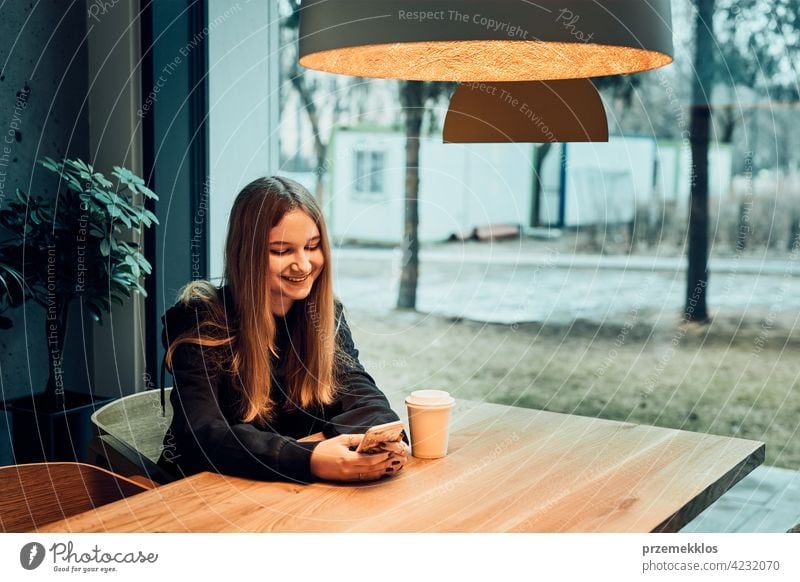 Young woman having a video call, talking remotely, drinking coffee, sitting in a cafe. Girl relaxing in cafe using mobile phone buy person restaurant caucasian