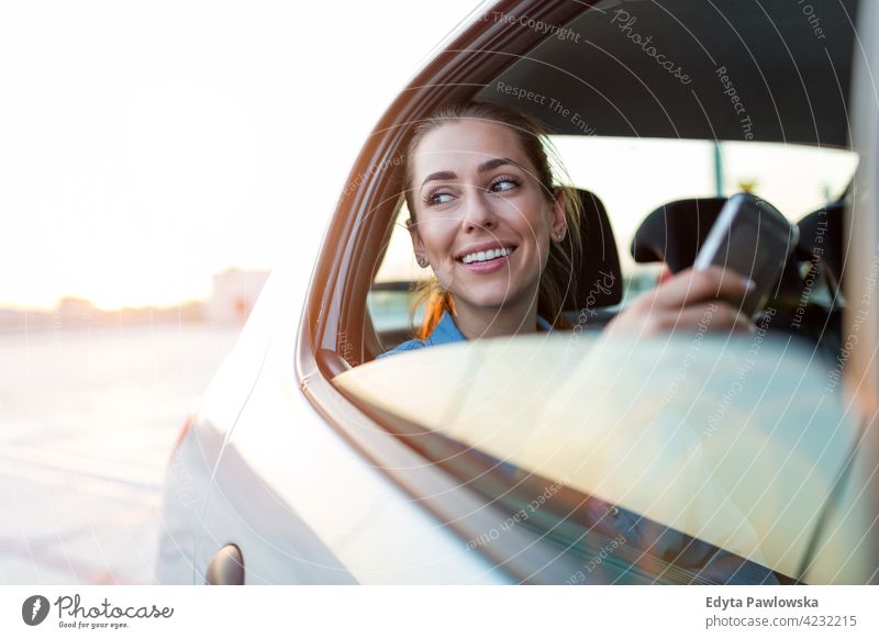 Young woman with smartphone on the back seat of a car carsharing confident smiling satisfaction female attractive beautiful young adult joy positive content