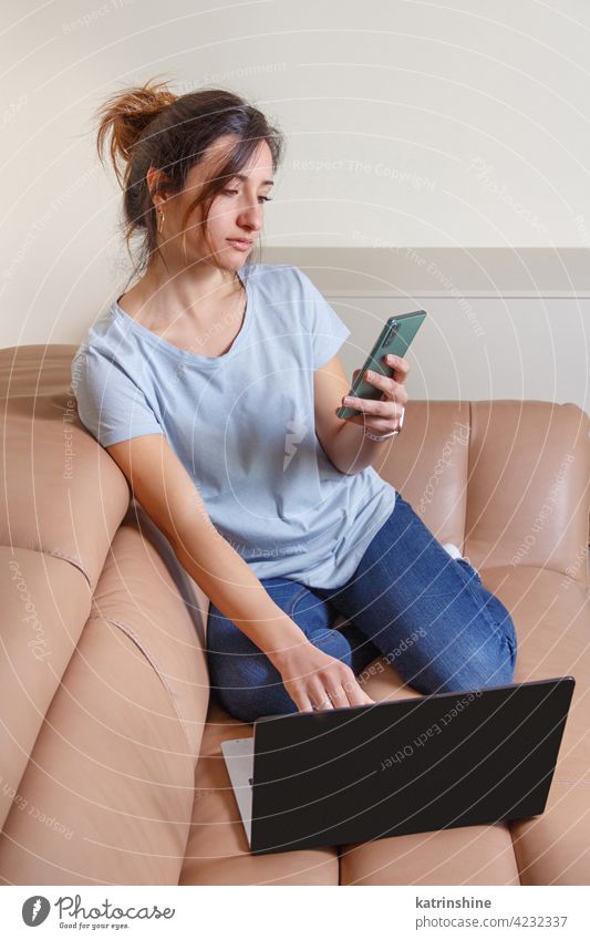 Young women working with laptop and using cell phone sitting on the sofa wear mockup t-shirt learn student Lifestyle jeans coffee to go cup serious concentrated