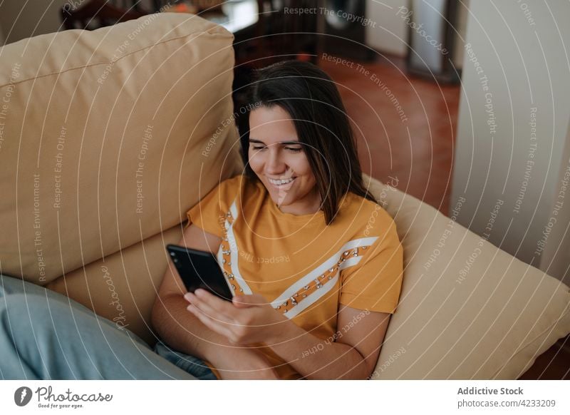 Woman chatting on smartphone on sofa at home woman internet house using gadget device smile lifestyle lying down cellphone happy text messaging delight watching