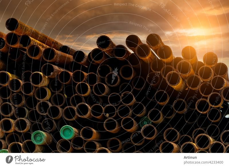 Pile of old rusty round metal industrial pipe. Steel pipe stack during sunset. Industrial material. Metal corrosion. Stack of round rusty tube abstract background. Old iron pipe warehouse of factory