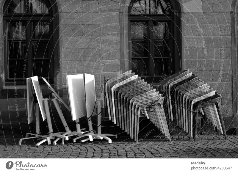 Stacked designer chairs and folded tables in front of an old café on the Römerberg in Frankfurt am Main in Hesse, photographed in neo-realistic black and white