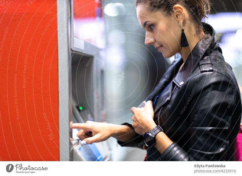 Young woman withdrawing money at an ATM atm machine bank banking finance cash credit card urban street city active people young adult casual attractive female
