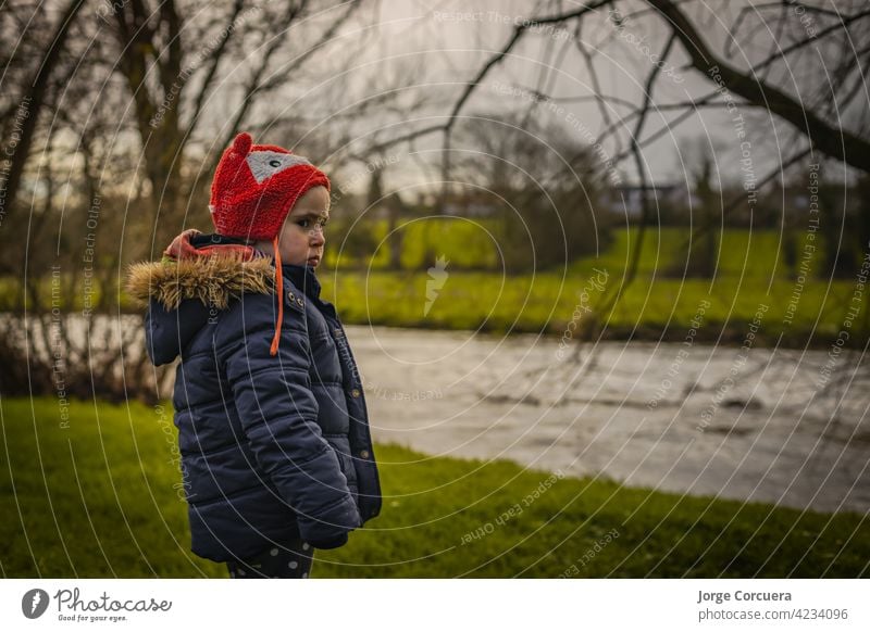 Two year old girl looking out over a river in a rural Irish outdoors setting. Dressed in winter clothes, big coat and warm hat. people young portrait female