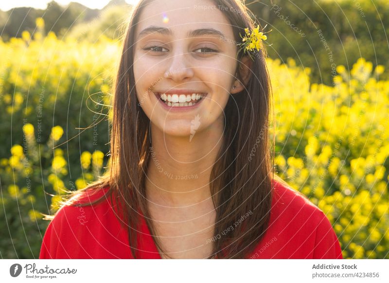 Crop happy woman with blooming flower in hair in sunshine toothy smile candid friendly blossom field countryside portrait summer natural plant bright red outfit