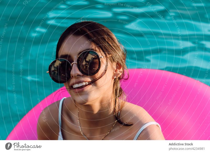 Content tourist in swimsuit resting in rubber ring in pool woman cheerful swimwear sunglasses vacation feminine traveler tender happy smile content glad