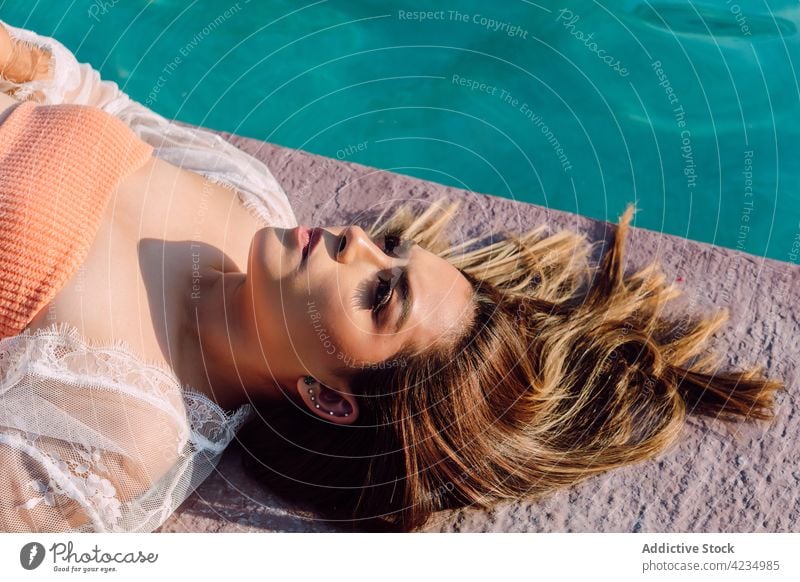 Traveler in earrings resting on poolside during trip tourist wistful feminine alone vacation reflective woman portrait traveler journey swimming accessory water