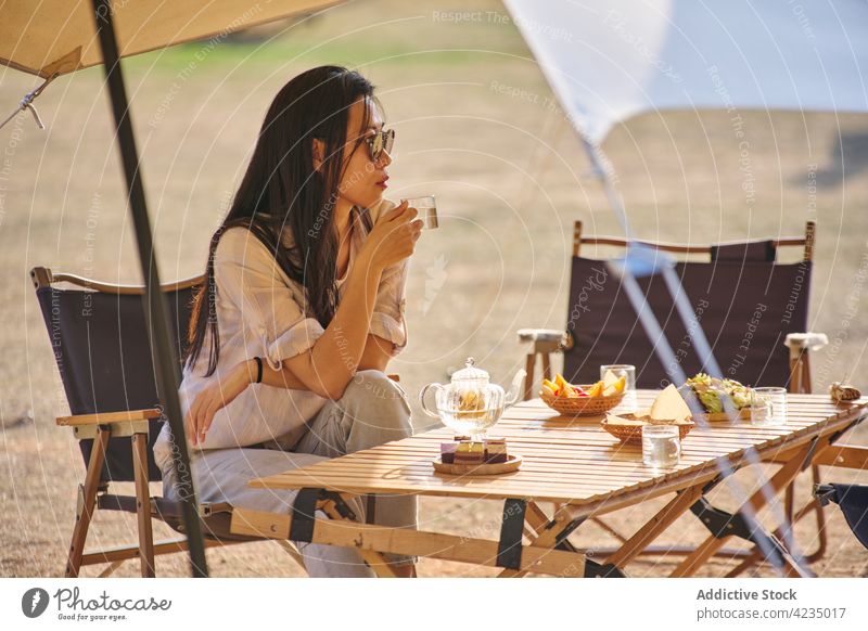 Asian woman having a relaxing time in camping area picnic tent summer ethnic sunglasses model female Chinese one person enjoy drink sunny nature grass alone