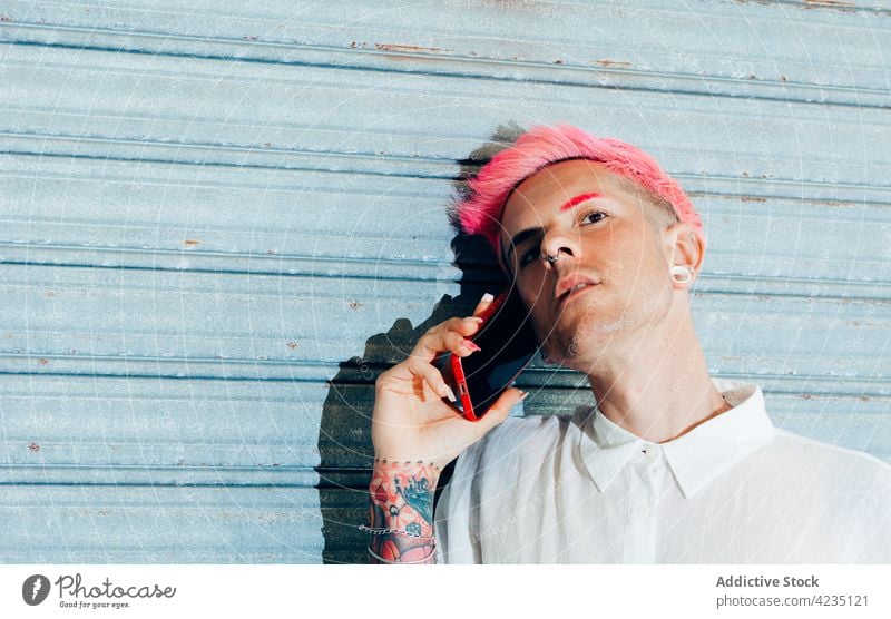Stylish gay speaking on smartphone on blue background fashion style tattoo cool individuality portrait using gadget device man piercing accessory earring