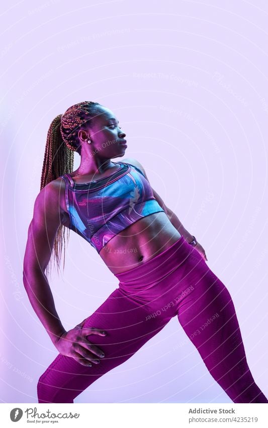 Fit black sportswoman in activewear on blue background athlete muscular body hand on hip self confident strength determine portrait power self assured bicep