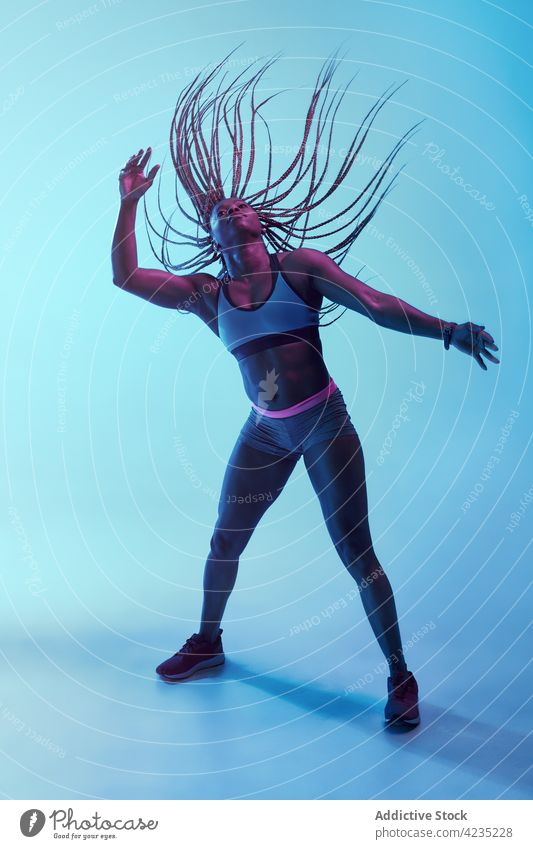 Black sportswoman with flying hair on blue background motion power afro braid muscular energy dynamic vitality sneakers modern style belly bicep muscle black