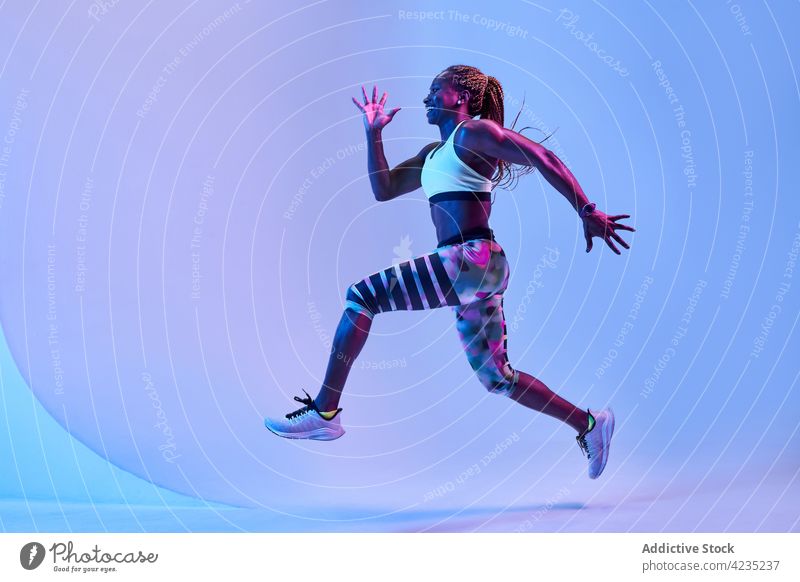 Active black sportswoman running in neon light jump activity fast training workout determine energy dynamic runner cardio leap exercise practice active rapid