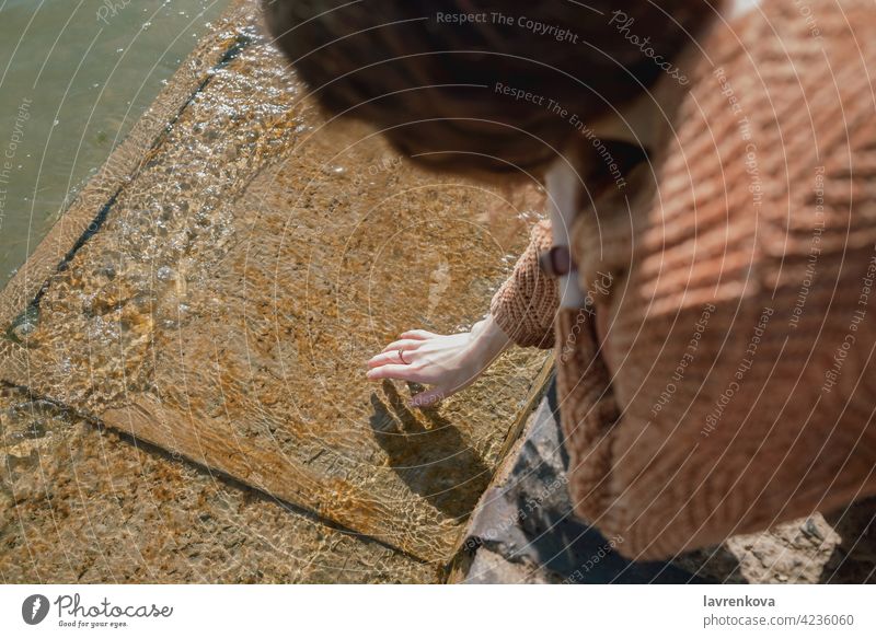 Woman touching cold water on a pier hand female faceless beach element clean clear sweater ripple nature outdoors peaceful lake lifestyle sea river waves close